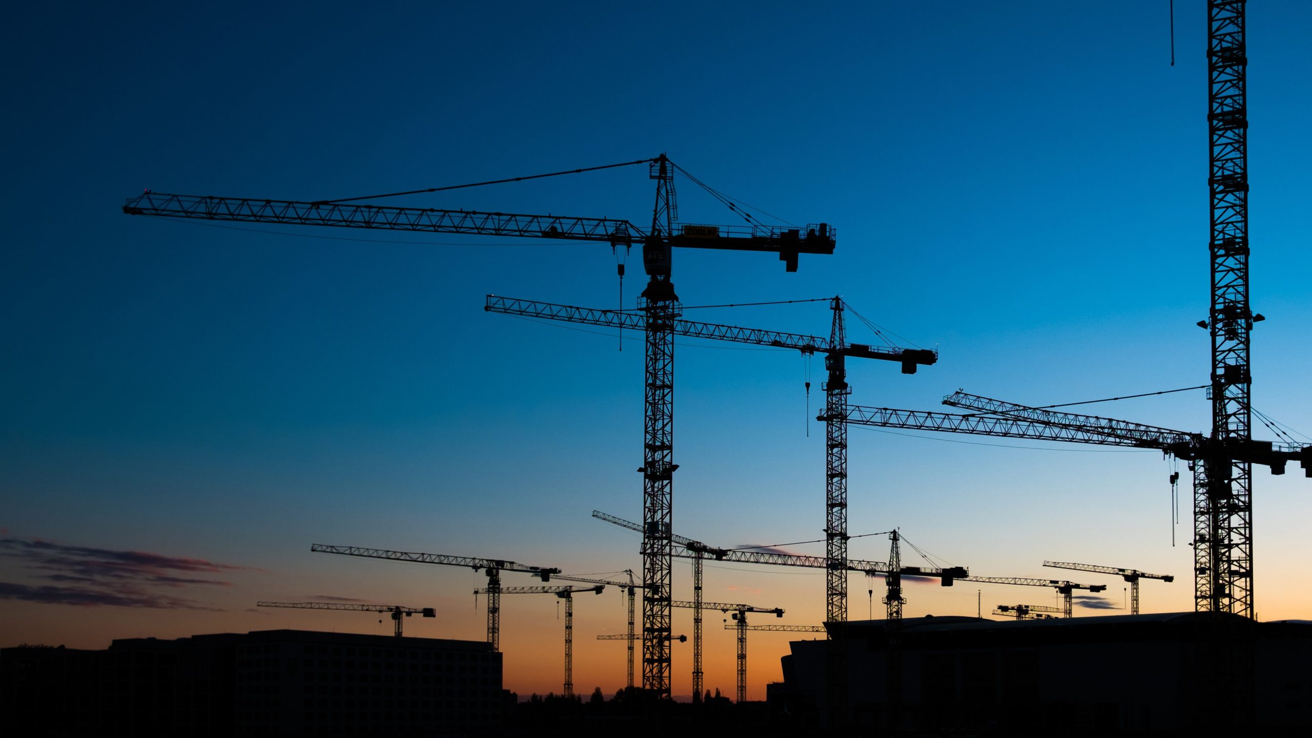 The silhouette of tower cranes on a construction site at sunset.