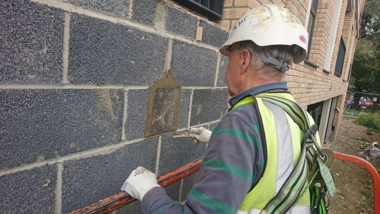 A bricklayer working from a cherry picker repairs blockwork on a London construction site