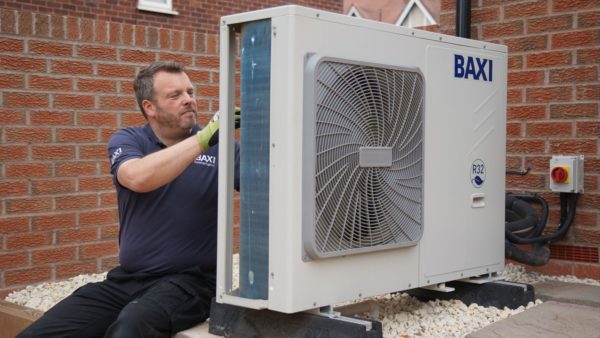 A male installer in a blue shirt working on a Baxi heat pump outside a red-brick house (Image courtesy of Baxi)