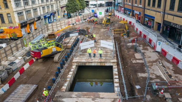 Aerial shot of the uncovered dock feeder canal in Churchill Way, Cardiff. Three individuals in hi-vis stand close to the open canal with an excavator's arm arched behind them (Image courtesy of Atkins)