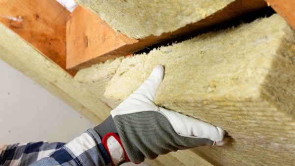 A worker's hand installing mineral wool insulation into a roof space