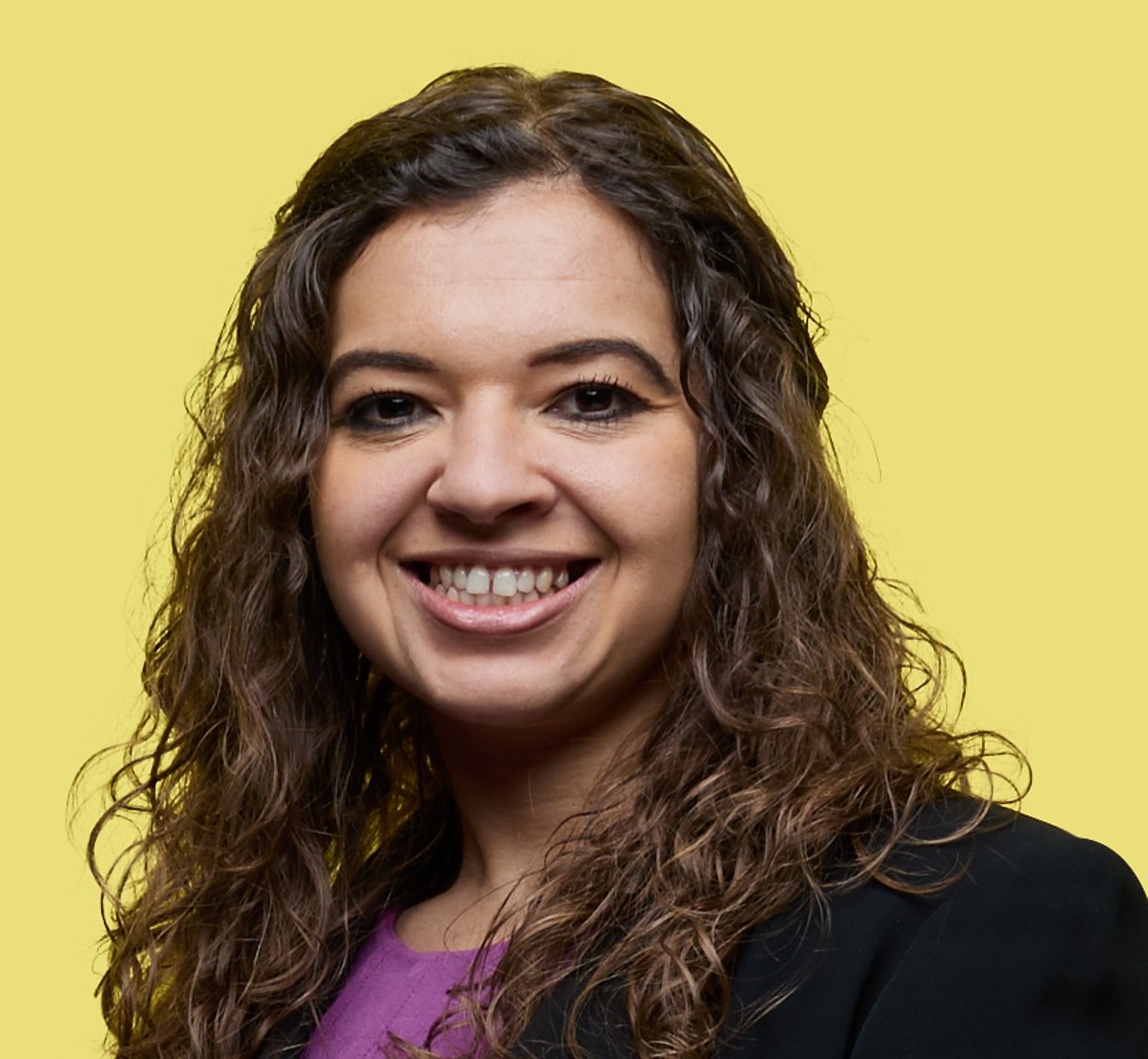A woman smiling at the camera with a yellow background.