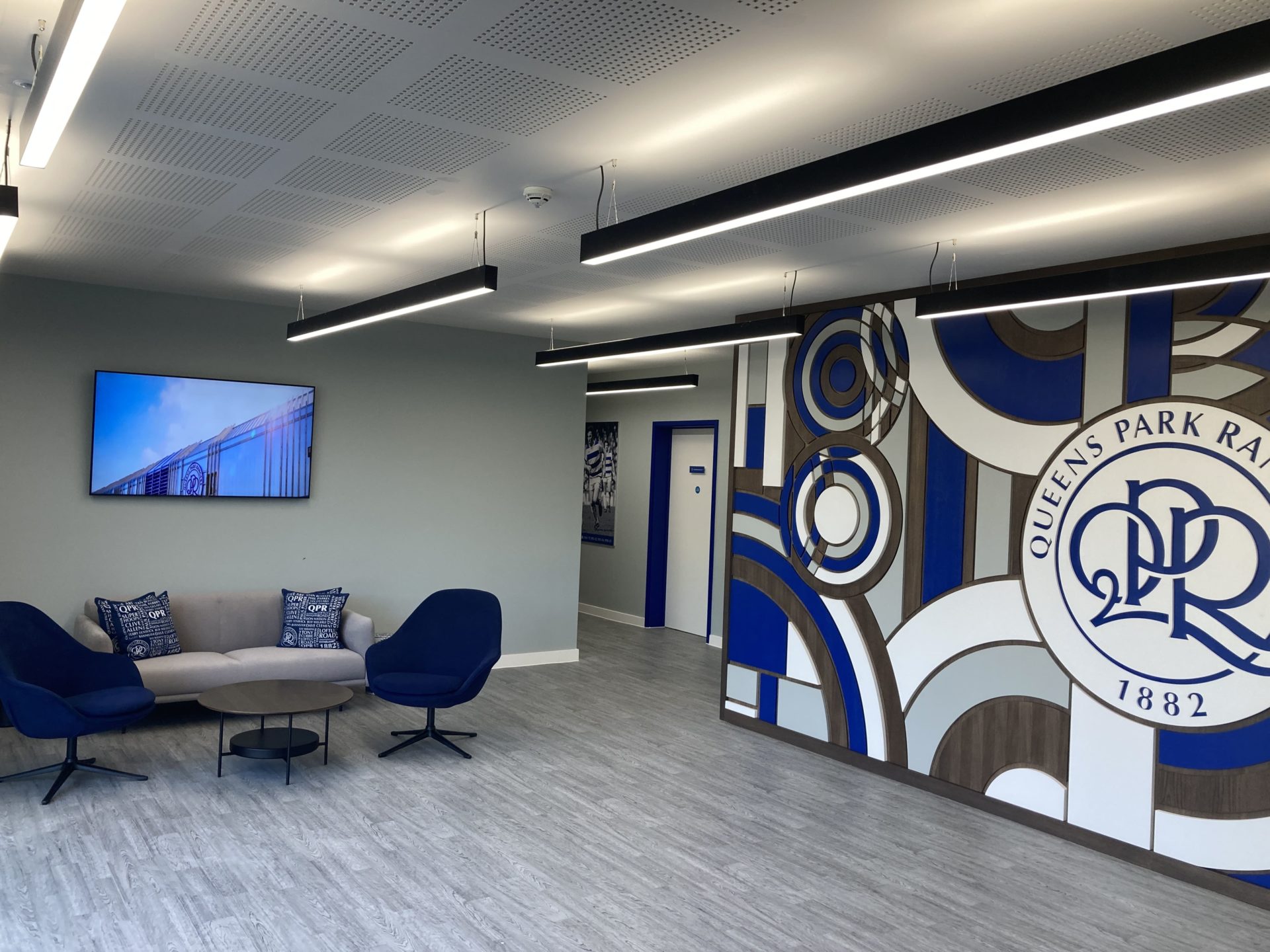 Buro Happold QPR - A lobby with a table, two chairs, a sofa an a TV.