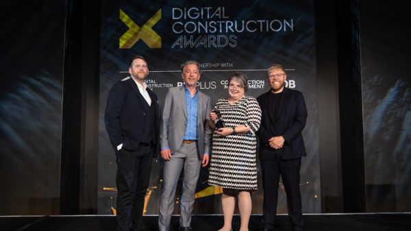Three men and one woman on a stage. The woman is holding an award.