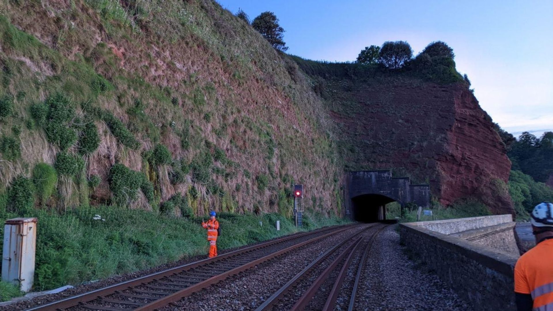 BAM coastal railway - Railway tracks heading towards a tunnel and two workers with orange high-vis jackets.