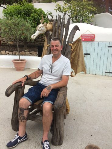 Photo of a man smiling at the camera and seated at a throne looking chair.