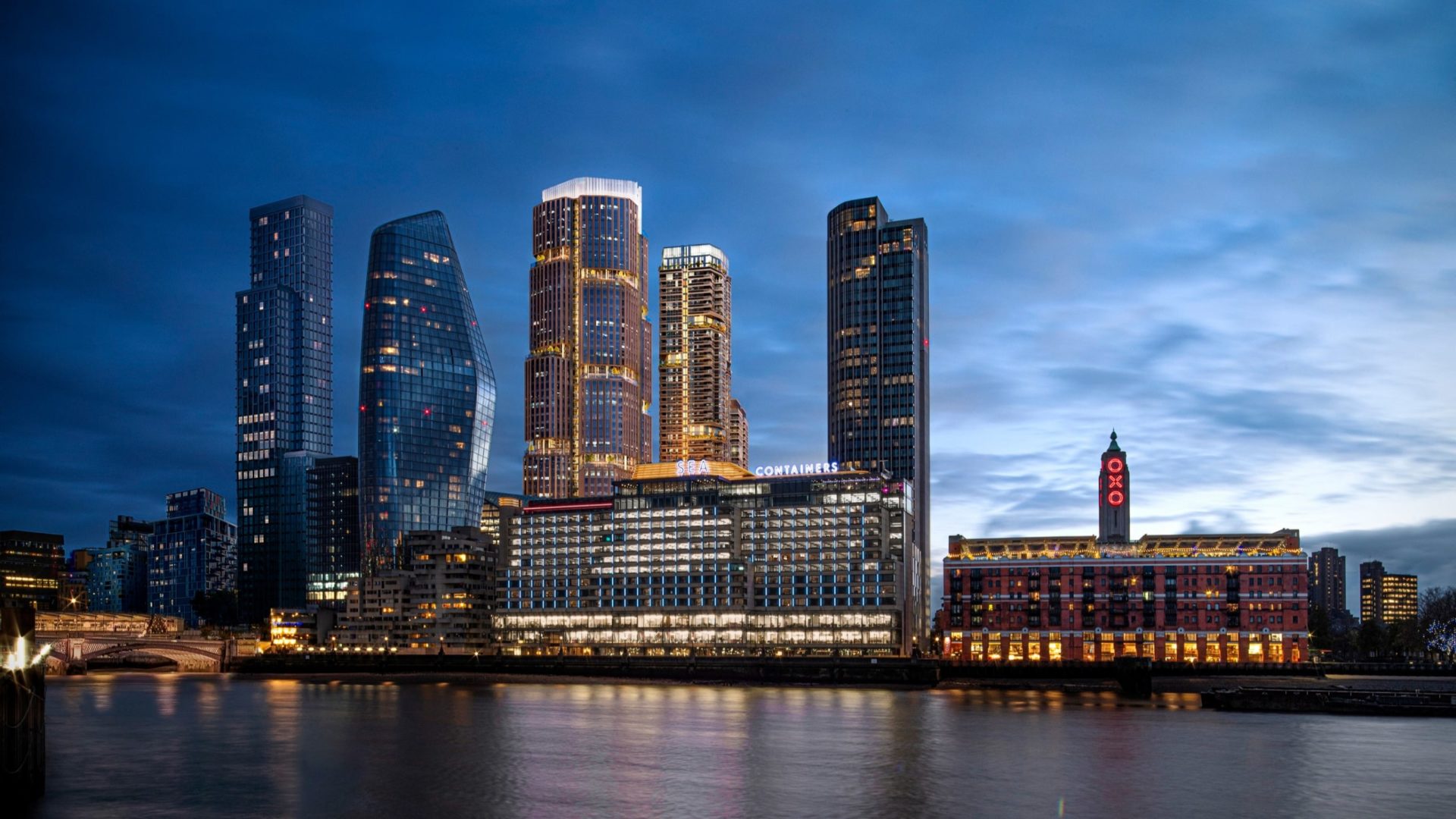 A night skyline of tall blocks in a city and a river.