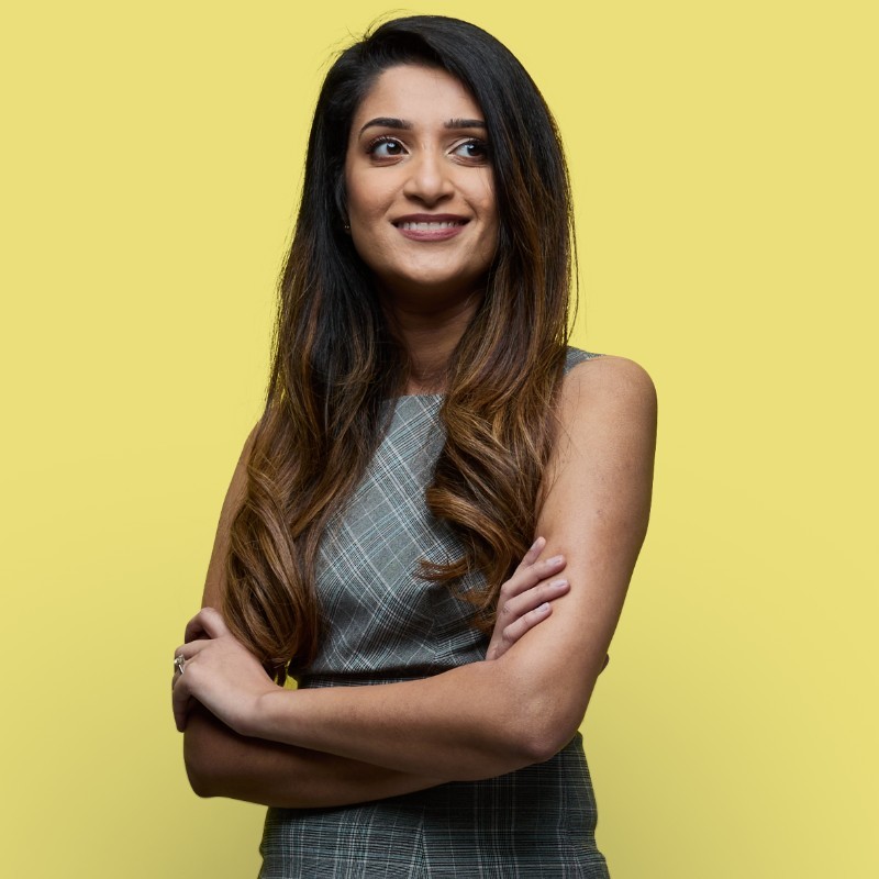 A woman smiling with her arms crossed on a yellow background.