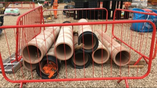 A bunch of heavy drainage pipes behind red fences.