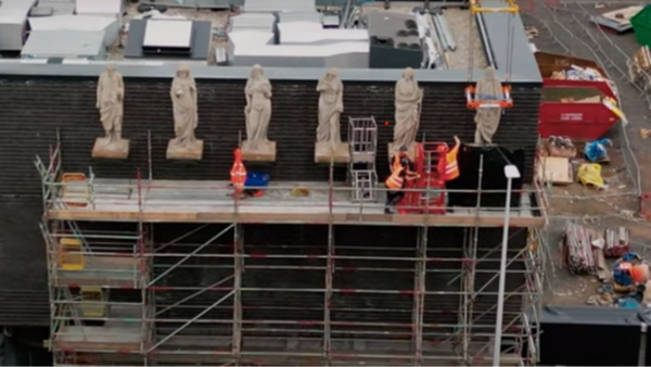 Workers on scaffolding working with six statues.