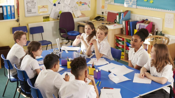 A classroom with school children sitting around a blue table.