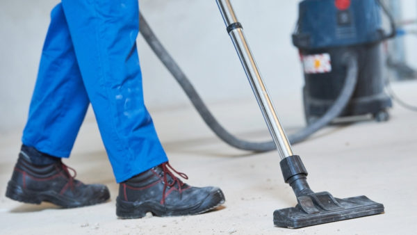 Construction worker (only their legs are seen) using a vacuum cleaner.