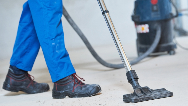 Dust inspections - Construction worker (only their legs are seen) using a vacuum cleaner.