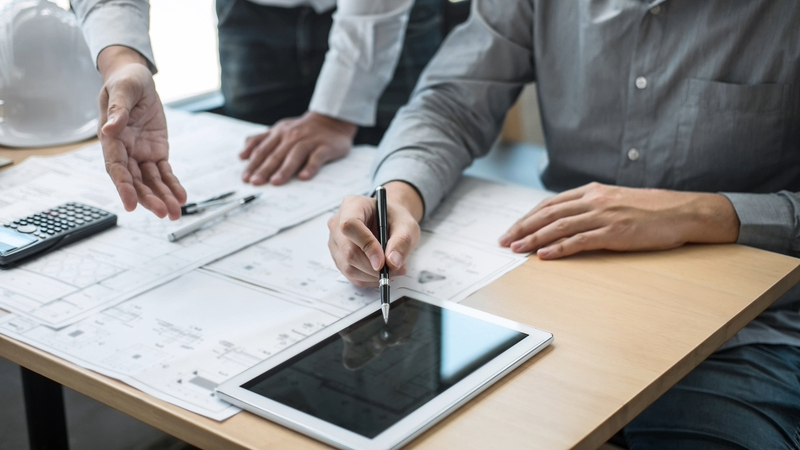 Construction engineering or architect discussing a blueprint and building model while checking information on sketching meeting