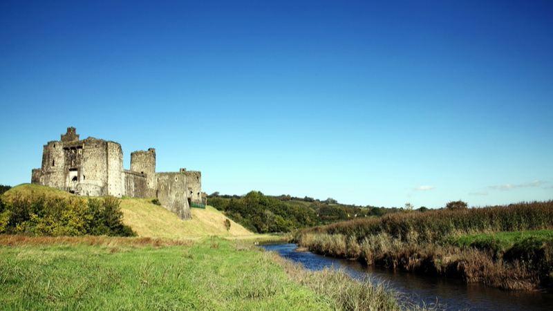 View of a field with a river and some castle ruins.