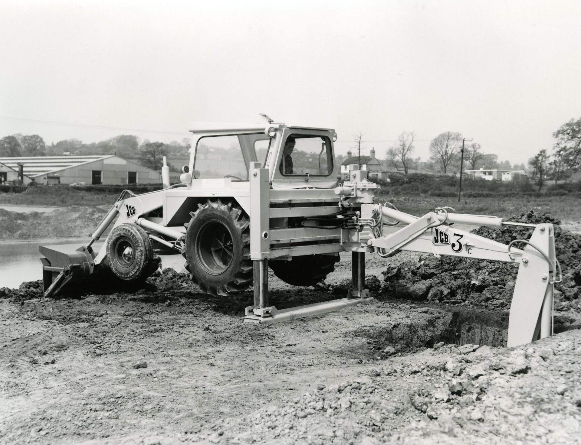 JCB backhoe loader - A black and white picture of an excavator in a field.