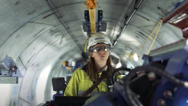 A woman with a hard helmet and PPE inside an underground tunnel operating machinery