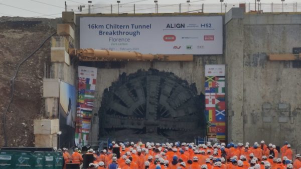 A giant machine breaking through the end of a tunnel and a big crowd assembling outside