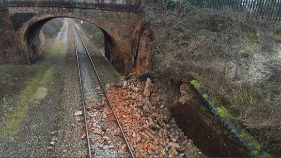 Train hits collapsed wall - View of train tracks with debris on them and a bridge in the background.