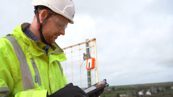 A man wearing personal protective equipment and using an electronic device.
