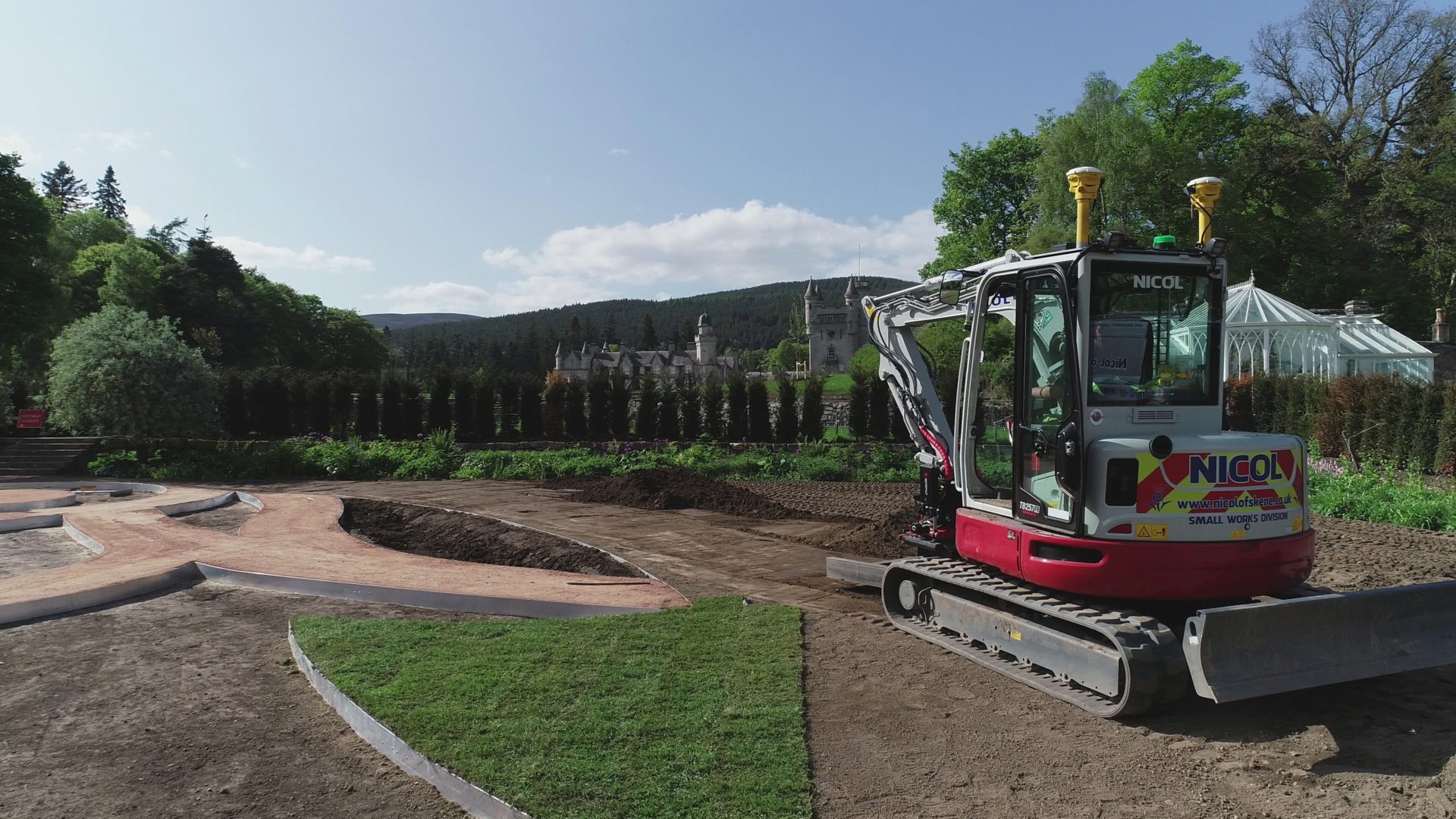 An excavator in a garden with a castle in the background.