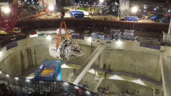 A tunnel boring machine lifted into place at a huge construction site at night.