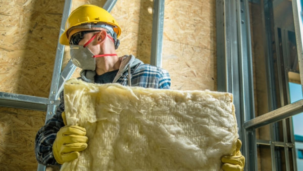 Construction worker wearing a safety mask moving pieces of mineral wool insulation. A new report by Turner & Townsend says that the UK is struggling to fill green-collar jobs.