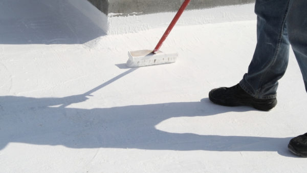 A worker applying roof coating to a roof using a broom. New research by UCL shows that a reflective coating would be more effective at cooling cities like London than vegetation-covered green roofs.
