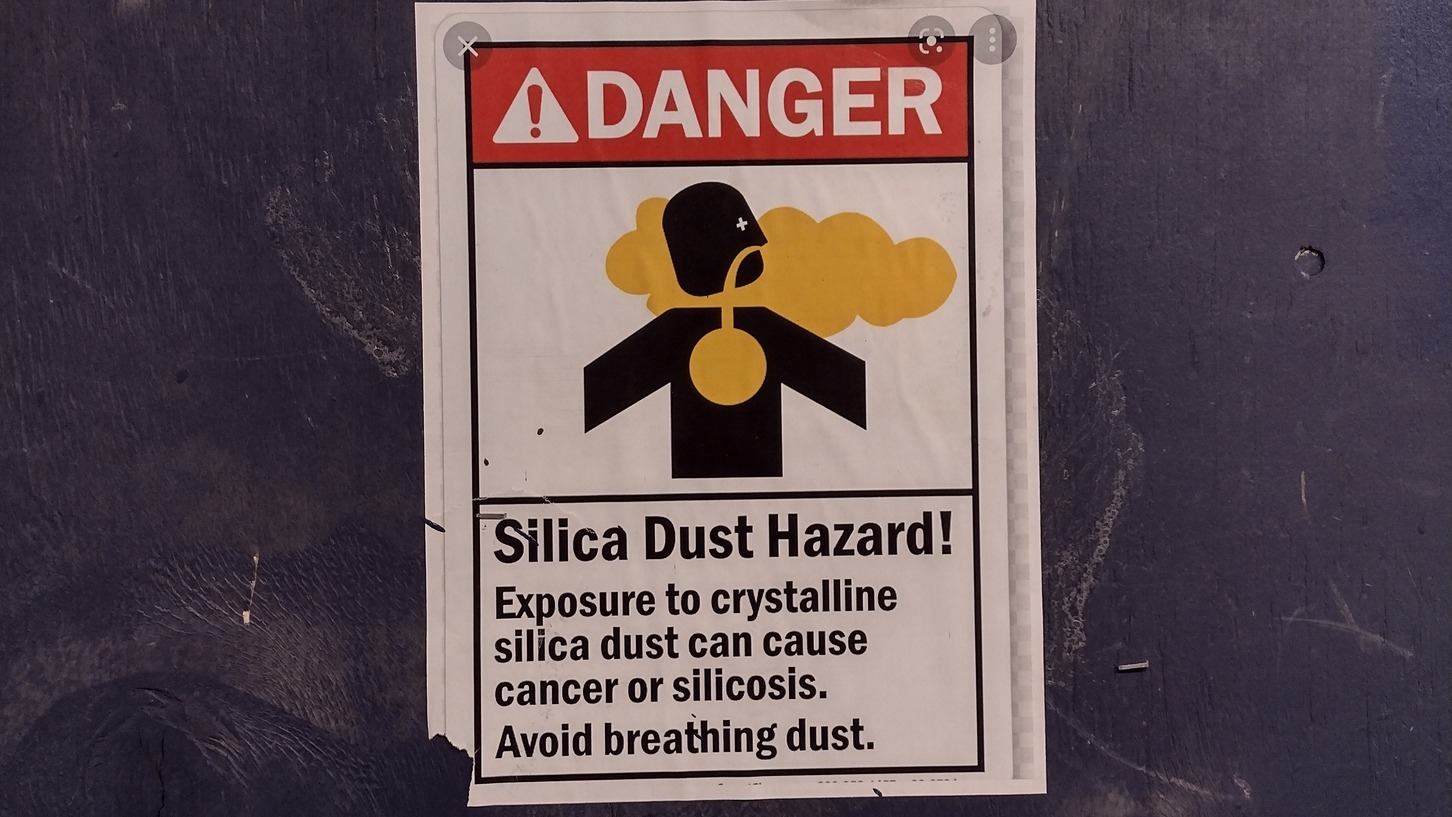 A sign which says 'danger, silica dust hazard!' with a human depicted inhaling yellow dust. A toolkit raising awareness of silica dust risk has won the first CIOB Paul Dockerill Award.