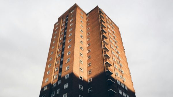 View from below of a tall brick residential block of flats - lawyers explain in this article steps that have been added to extend the definition of remediation under the Building Safety Act 2022