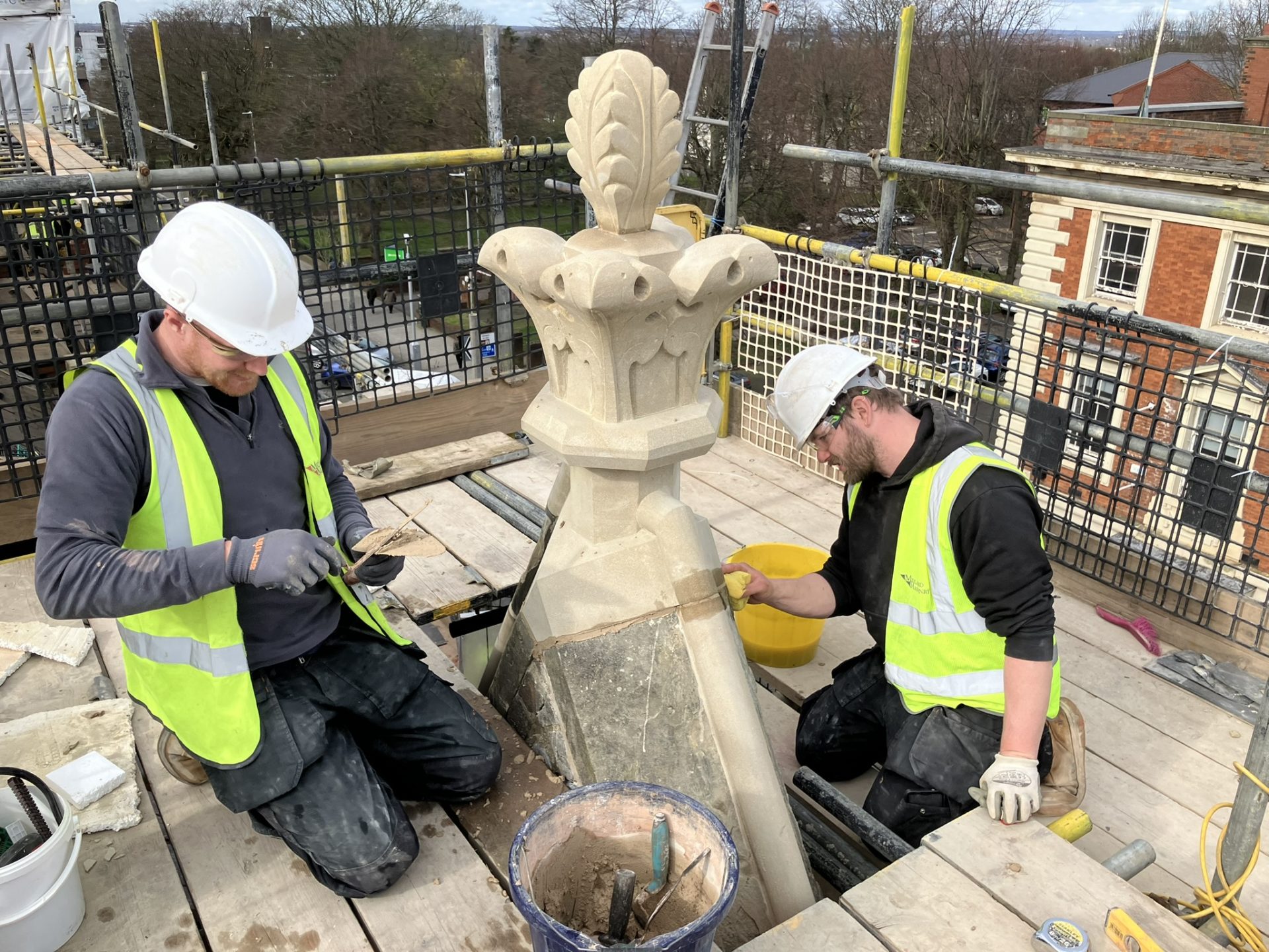 Two workers with hard helmets and high-vis jackets restoring an element of the town hall