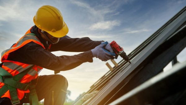 Technician roofer in a protective uniform working on a roof with an electric drill. Roofers have reported heavy losses following ISG's collapse.