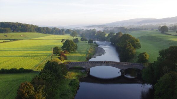 A river surrounded by green fields and trees. There's an aqueduct crossing it. A consortium made of Strabag and Equitix has been named preferred bidder to deliver Haweswater Aqueduct Resilience Programme.