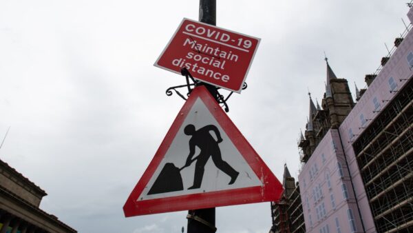 Two street signs. Top sign reads Covid 19 Maintain social distance and lower sign is a construction site caution sign. BSI is calling for evidence on experiences of Covid career starters in the built environment