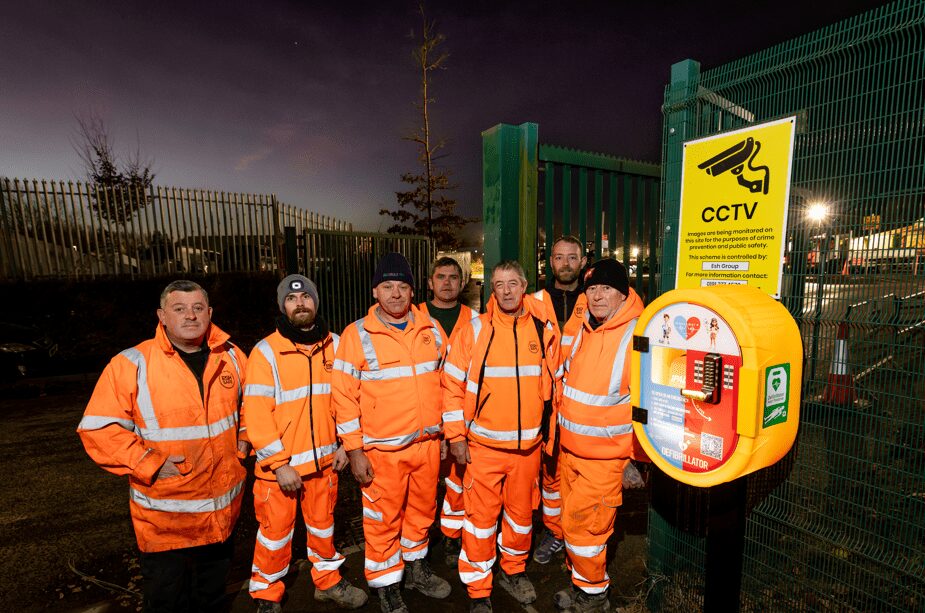 Esh defibrillators - A group of workers wearing orange high-res clothes next to a defibrillator - Esh Group has installed 55 of these machines across its sites