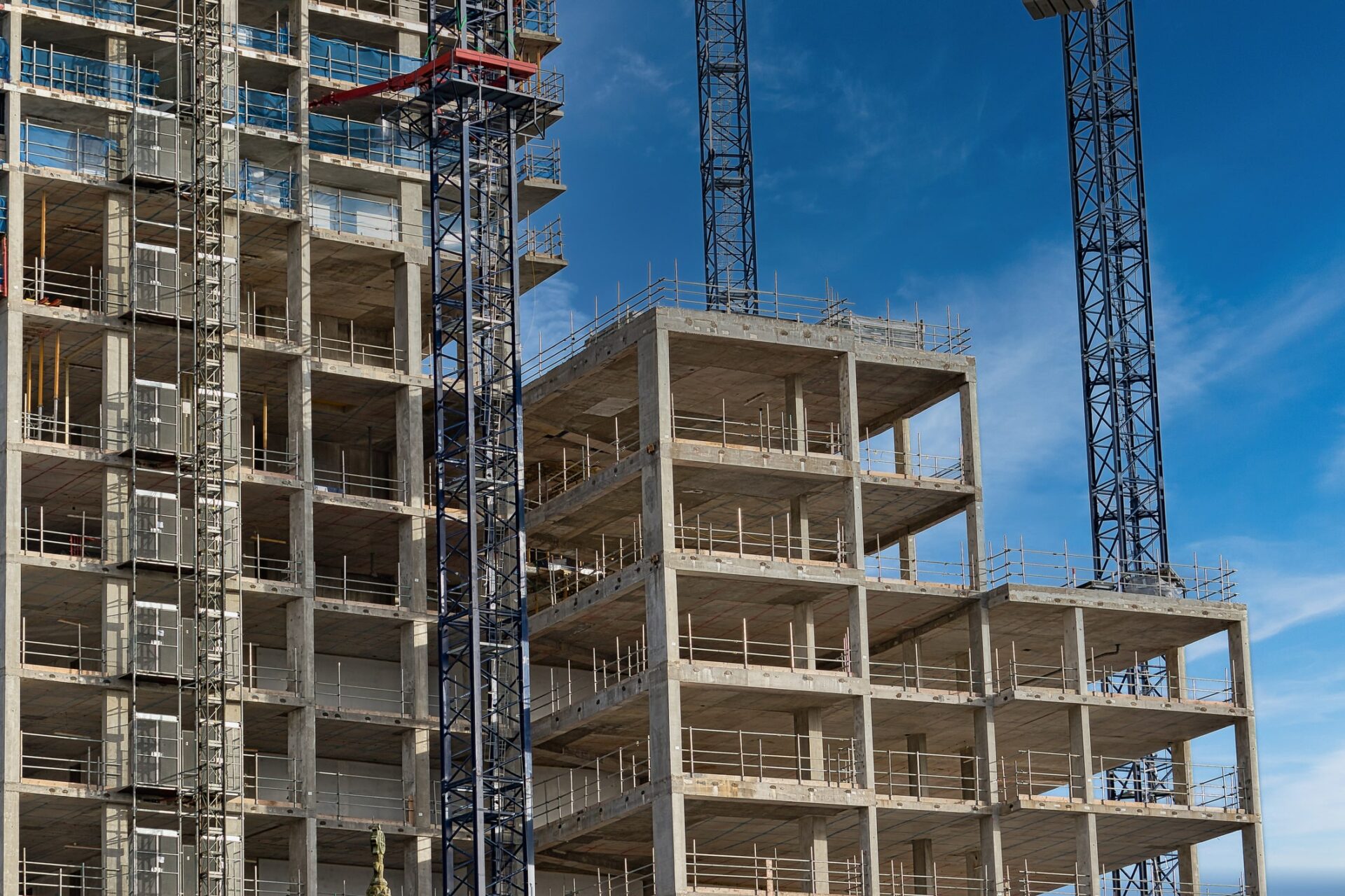 High-Rise building construction site with cranes and scaffolding. Two adjacent high-rise buildings under construction are visible against a clear blue sky. Adrian Gladstone writes that the Building Safety Regulator will need more resources to deal with the delays of the gateways process.