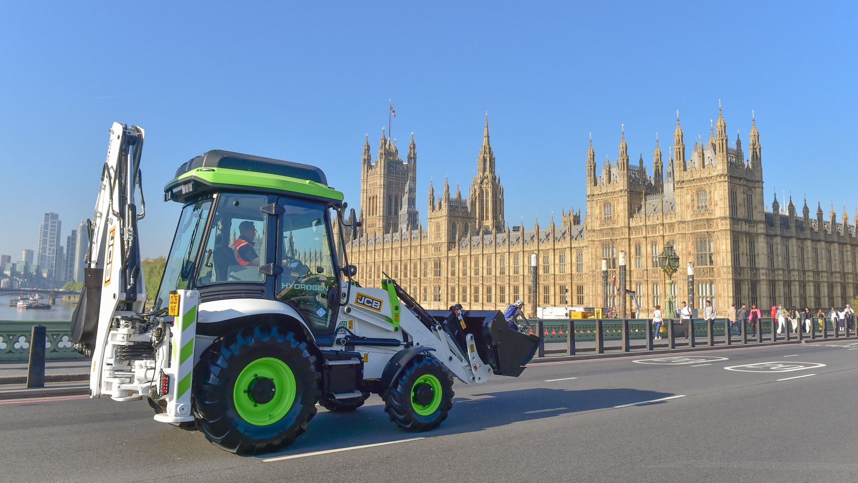 A green digger with the Houses of Parliament in the background - the government has changed the law to give hydrogen diggers the green light to be driven on UK roads.
